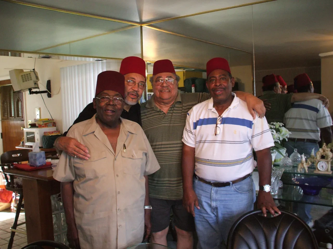 Four men wearing red fezzes indoors